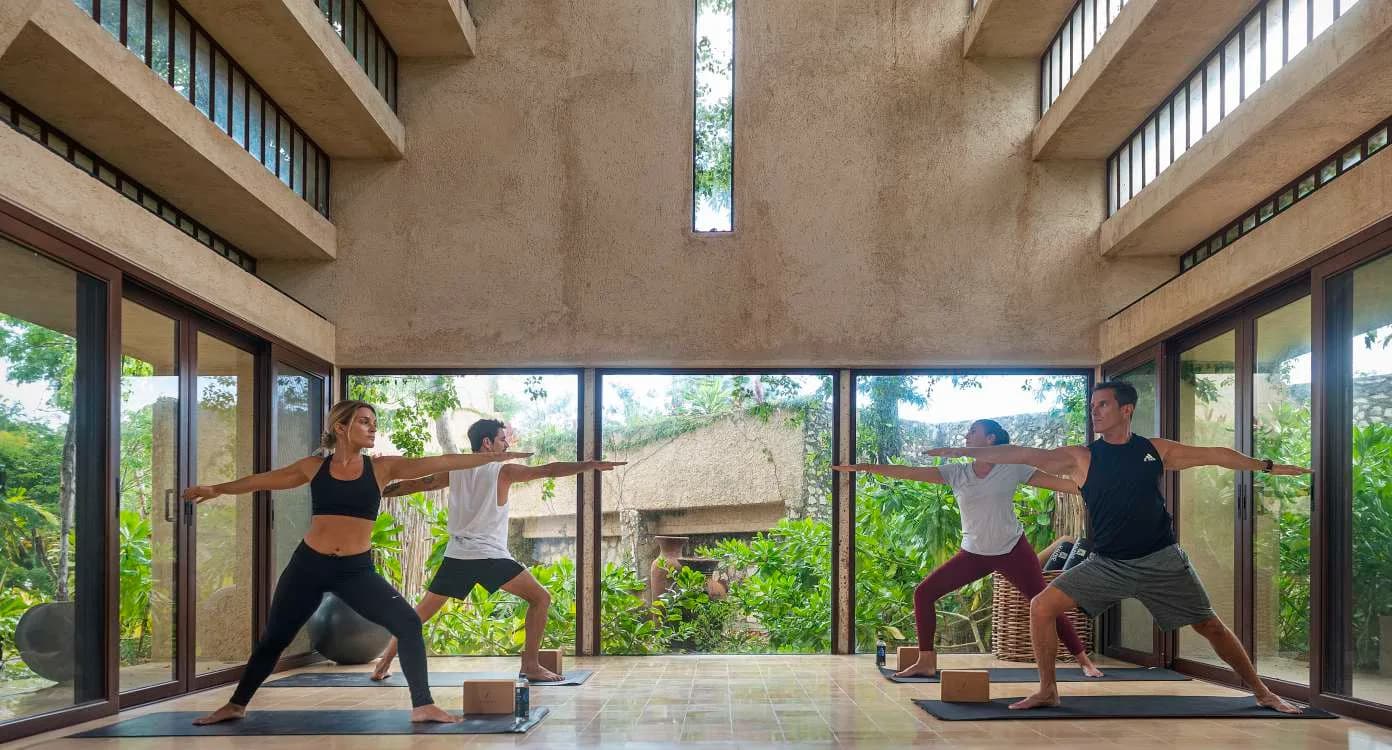 Clase de yoga en el salón de doble altura con ventanales hacia la selva